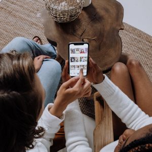 Two people looking at social media on a smartphone at a wooden table.