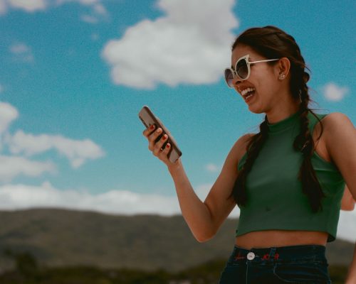 woman in green tank top holding smartphone during daytime